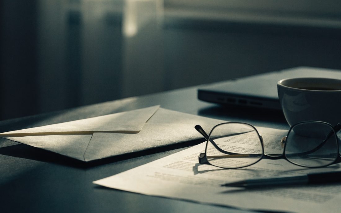 Sobre oficial sellado y un oficio impreso sobre un escritorio, junto a lentes de lectura y una taza de café