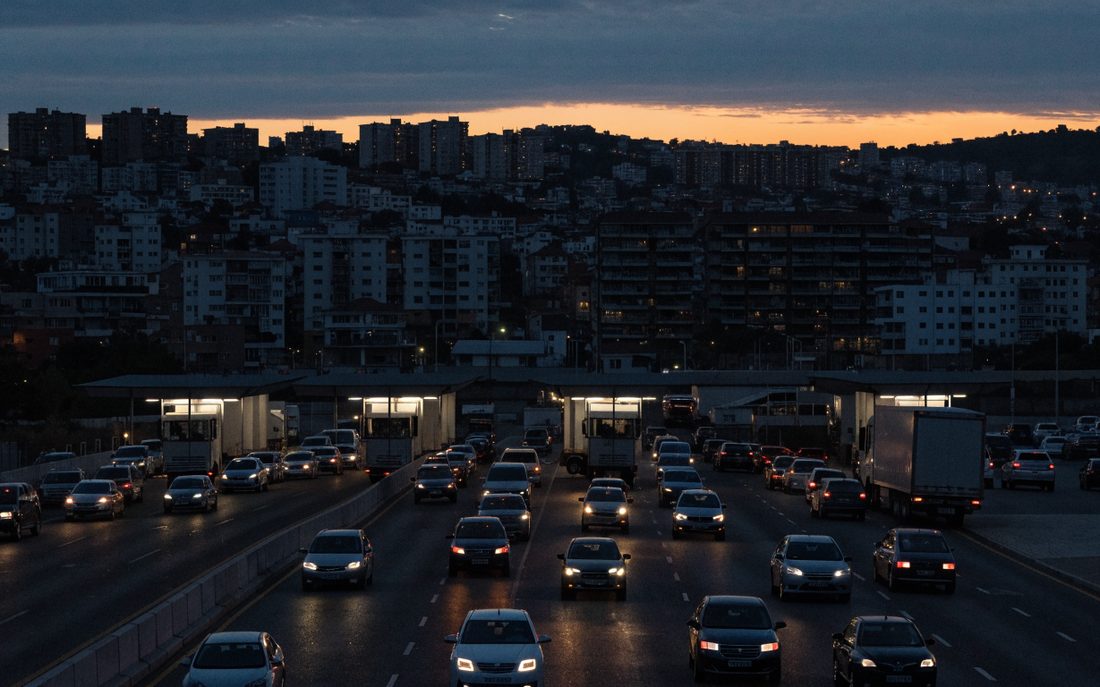Cruce fronterizo entre Tijuana y San Diego al anochecer, con filas de autos y tráileres bajo las cubiertas de inspección