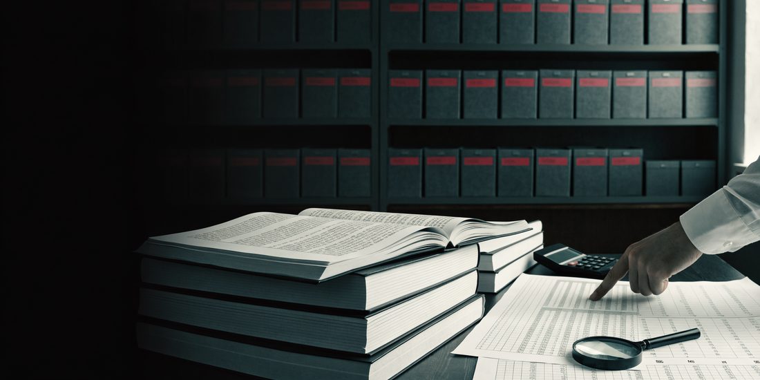 Mesa de auditoría con libros contables abiertos, papeles de trabajo marcados, lupa y cajas de archivo
