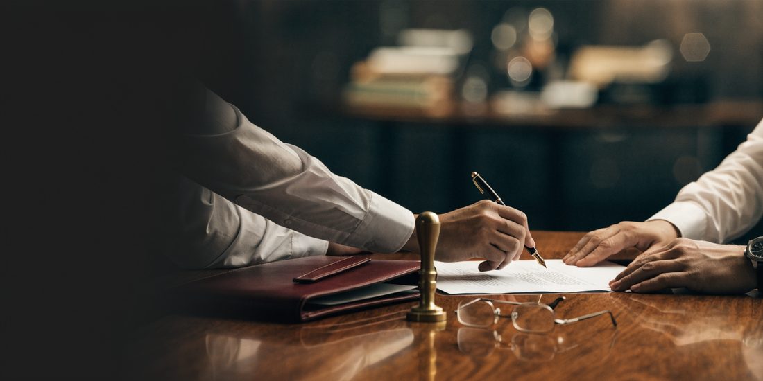 Firma de un acta constitutiva sobre una mesa de madera, con sello notarial y carpeta de piel vino