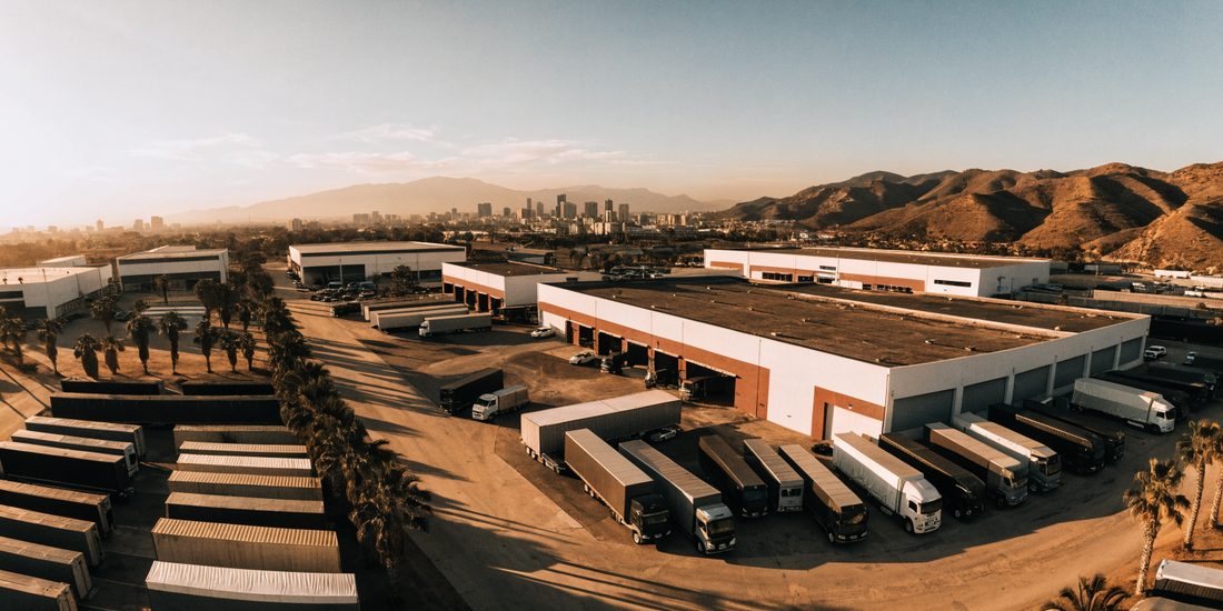 Parque industrial de Tijuana al atardecer, con naves, andenes de carga y tráileres